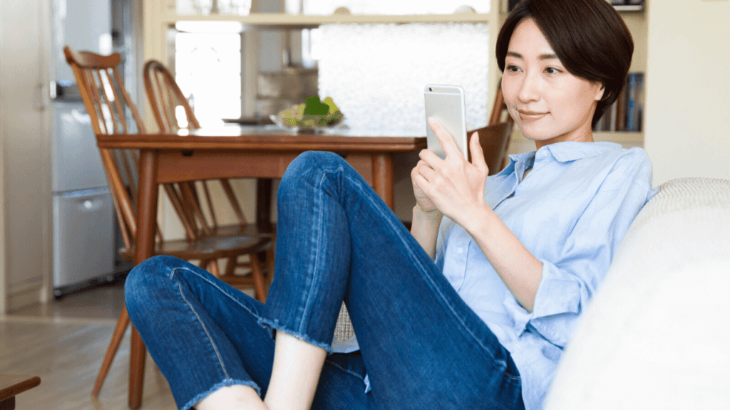 ソファーに座りスマホで物件情報を調べる女性