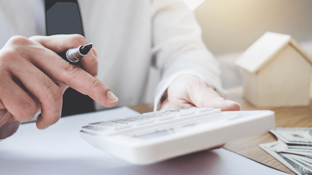 家の模型の前で電卓をたたく男性